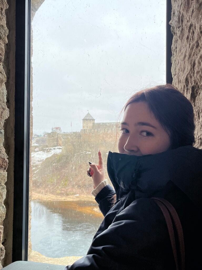 A young woman looks at the camera and points out a window across a river.